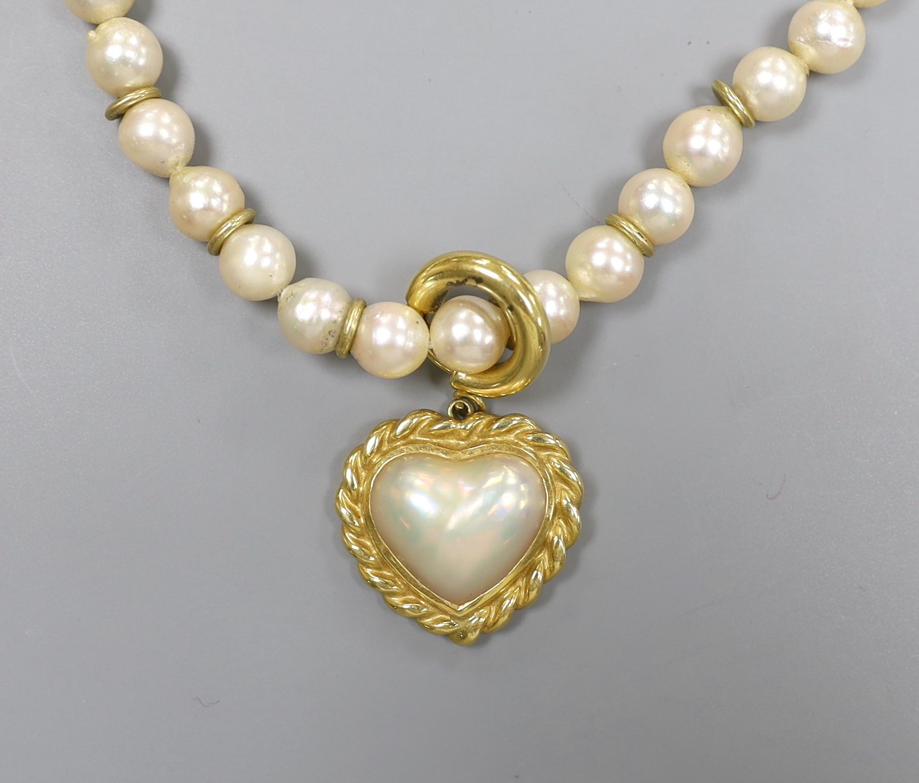 A 1960's single strand cultured pearl necklace, with an 18ct gold and mother of pearl set heart shaped pendant, necklace 39cm, pendant 25mm, gross weight 62.1 grams.